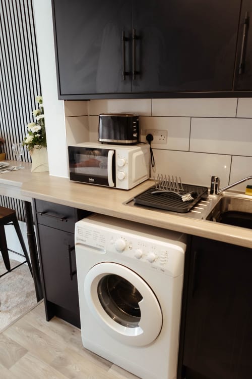 Modern kitchen area in The Snug apartment featuring white washing machine, microwave, toaster, and compact appliances at JS
