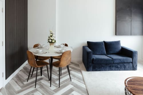 Modern apartment living area at JS Apartments Blackburn with dining table, brown chairs, navy sofa, and herringbone flooring.