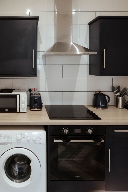 Modern kitchen in JS Apartments Blackburn with stainless steel range hood, black cabinets, white subway tiles, and integrated