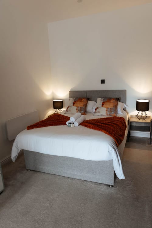 Modern bedroom in The Spacious Suite at JS Apartments, Blackburn with gray upholstered bed, red throw, and ambient lighting