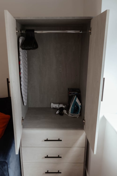 Open wardrobe with hanging rail, iron, and ironing board in JS Apartments Blackburn suite