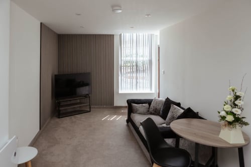 Modern living area at JS Apartments' Family Flat in Blackburn with black sofa, TV, dining table and city views