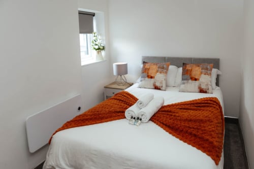 Modern bedroom at The Family Flat, JS Apartments in Blackburn, featuring orange throws and white bedding