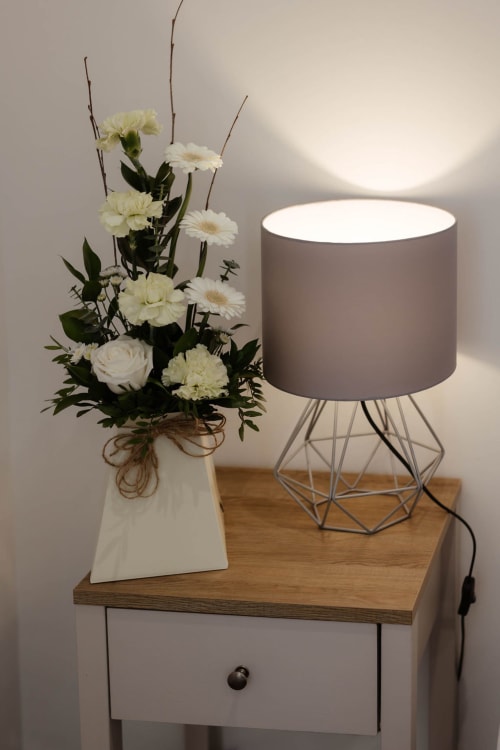 Bedside table in The Family Flat with white flowers, modern lamp, and wooden drawer in Blackburn apartment