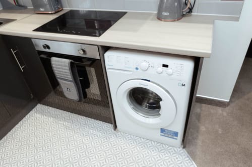Modern kitchen at JS Apartments Blackburn featuring white inset washing machine under cream countertop with black oven and