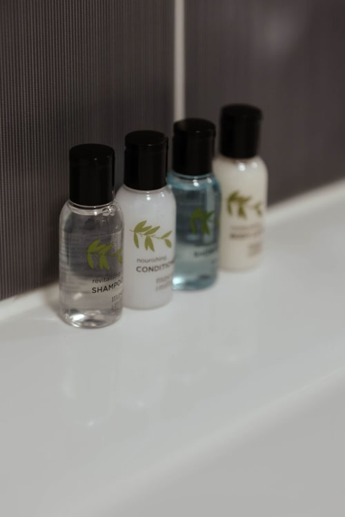 Four miniature hotel toiletries in black caps lined on white surface at JS Apartments Collection, Blackburn