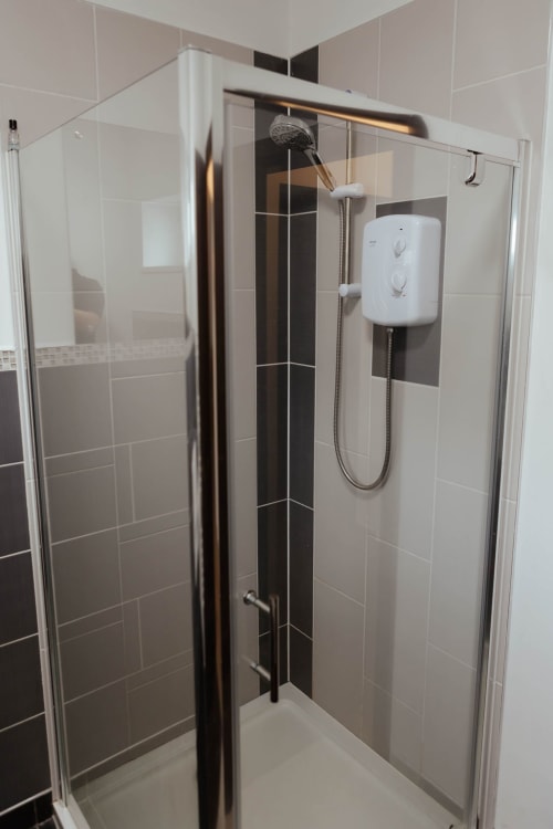 Modern shower enclosure with black tile accent wall and white electric heater in JS Apartments, Blackburn