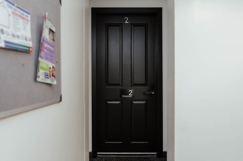 Black entrance door marked with number 2 at The JS Apartments Collection in Blackburn, with hallway notices on left wall