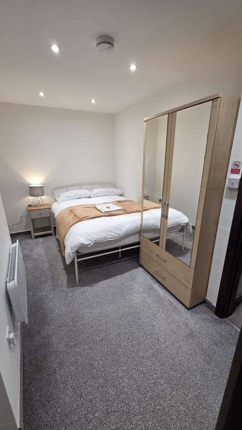 Modern bedroom at JS Apartments, Blackburn featuring bed, mirrored wardrobe, nightstand lamp and recessed ceiling lights
