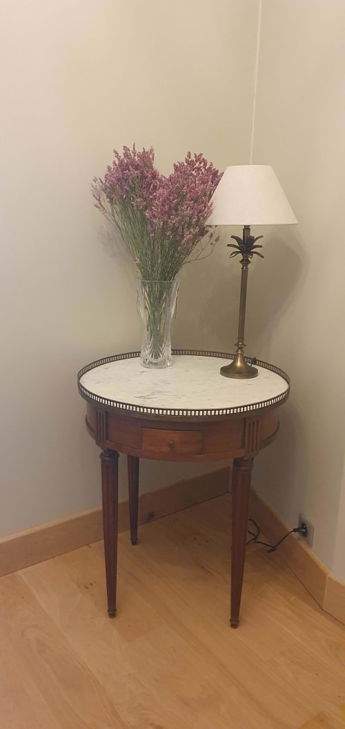 Table d'appoint ronde élégante en marbre et base bois, décorée de fleurs de statice violettes et lampe de table en laiton aux