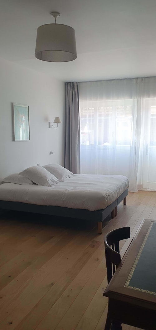 Chambre lumineuse à l'hôtel Les Cabines à Houlgate avec lit queen-size, luminaire suspendu et vue sur la ville par de grandes fenêtres