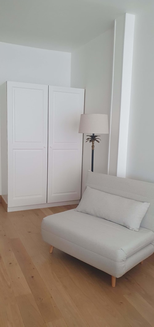 Chambre moderne de l'hôtel Les Cabines à Houlgate avec canapé blanc, armoire et lampadaire palmier sur parquet