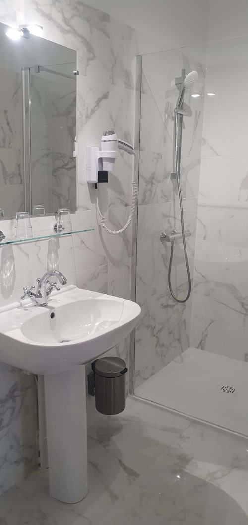 Salle de bain moderne aux carrelages à motifs marbre, lavabo blanc, miroir et douche vitrée à l'hôtel Les Cabines à Houlgate