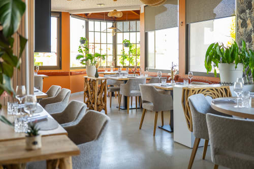 Modern restaurant dining room at Hôtel Restaurant Le S'Y in Seingbouse with orange accents, natural light, and potted plants