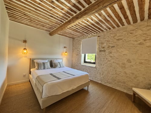 Chambre douillette du gîte Domaine Mas Lafleur à Châteaurenard avec poutres en bois, murs en pierre et luminaires suspendus chaleureux