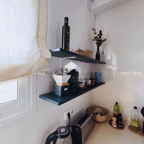 Estantería de cocina con unidad negra que exhibe aceite de oliva, jarrón decorativo y artículos de almacenamiento en la villa Barrosa Home