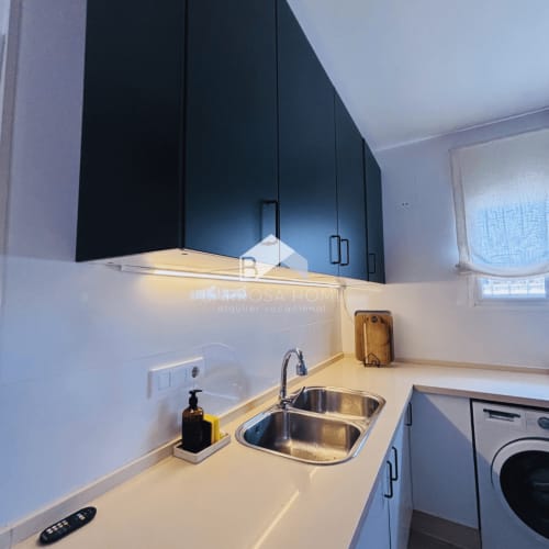 Cocina moderna con muebles oscuros, fregadero de acero inoxidable y encimeras blancas en la villa Barrosa Home de Hozanejos