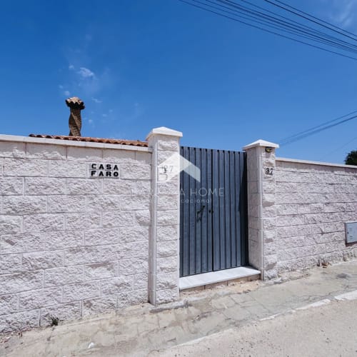 Entrada de la villa Casa Faro con muros de piedra blanca y puerta de hierro oscuro en Hozanejos