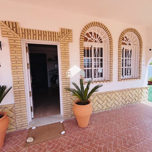 Entrada de Villa Faro con macetas de terracota, ventanas arqueadas y patio de ladrillo en Barrosa Home, Hozanejos