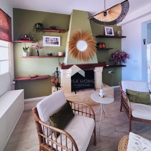 Moderna sala de estar en Barrosa Home Villa Faro con paredes verde oliva, espejo dorado de rayos solares, estantería y chimenea