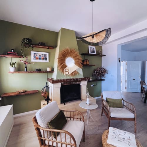 Sala de estar Villa Faro con paredes aceituna, chimenea, sillas de mimbre y vistas al jardín en Barrosa Home, Hozanejos