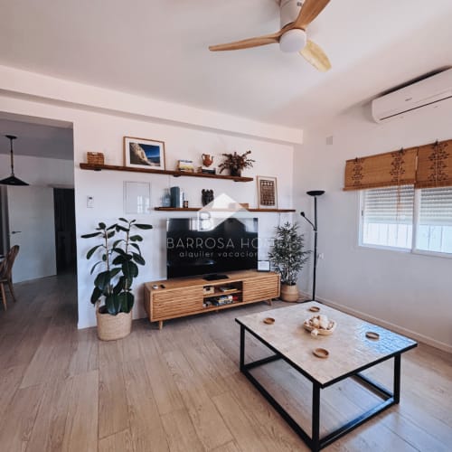 Moderno salón en Villa Faro de Barrosa Home con mueble de TV en madera, pantalla plana, plantas y mobiliario minimalista