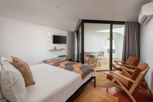 Modern studio apartment at Monte das Açoteias with bed, terrace access, wooden chairs, and TV in Tavira, Portugal