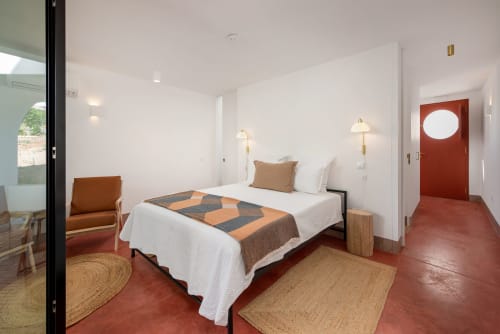 Modern studio bedroom at Monte das Açoteias with red terracotta floor, white bedding, bronze accents, and private entrance in