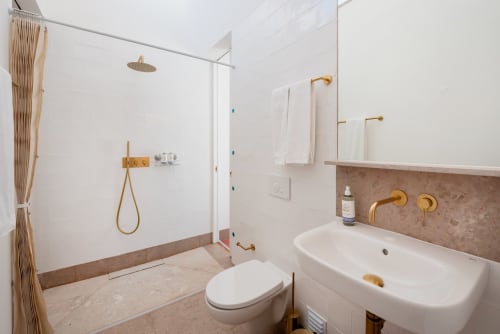 Modern bathroom at Monte das Açoteias with rainfall shower, gold fixtures, white tile walls, and marble accents