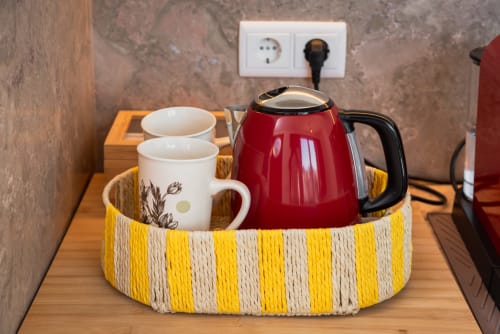 Red kettle and ceramic mugs in yellow striped basket at Monte das Açoteias studio kitchenette, Tavira