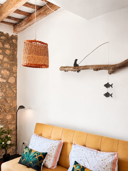 Acollidora habitació de l'hotel Mas Ribas a Palamós amb capçal groc, làmpada penjant teixida i mòbil artístic de fusta flotant