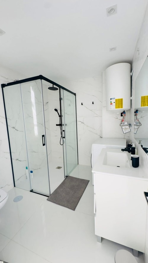 Baño moderno con ducha de mármol, tocador blanco y calentador de agua en el hotel ALTOVELOO MAR de Torre de Benagalbón
