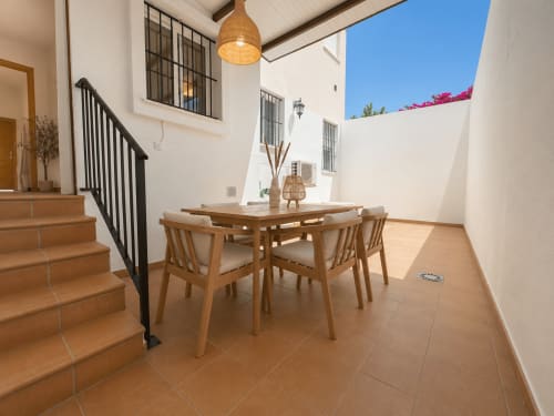 Soleada terraza de comedor en el apartamento Living Sur de Sanlúcar de Barrameda con mesa de madera, sillas y escalera