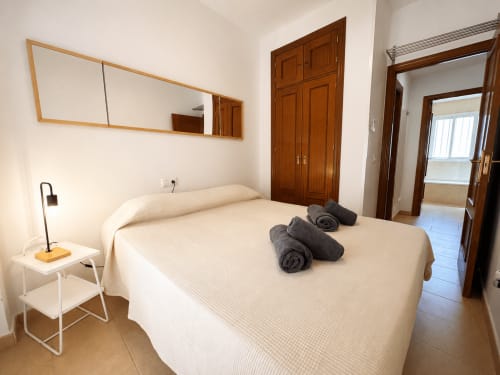 Dormitorio luminoso en el apartamento Living Sur de Sanlúcar de Barrameda con cama doble, toallas enrolladas, espejo, puertas de madera y
