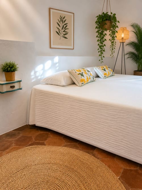 Bright bedroom at Mas Ribas Hotel with white bed, yellow patterned pillows, hanging plants, and coastal garden view in