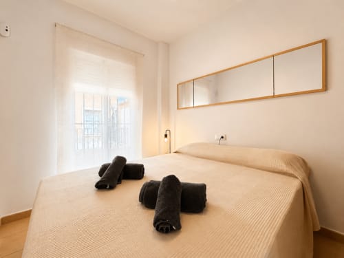 Dormitorio luminoso en apartamentos Living Sur de Sanlúcar de Barrameda con cama, toallas enrolladas, espejo y acceso a terraza