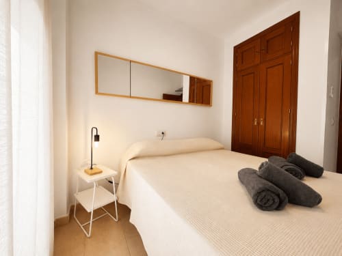 Dormitorio moderno en apartamentos Living Sur de Sanlúcar de Barrameda con cama, espejo, mesita de noche y toallas enrolladas