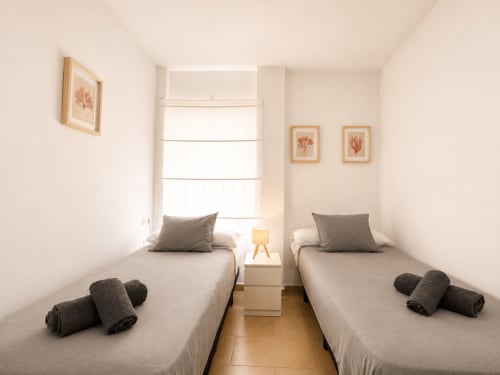 Habitación doble con toallas enrolladas en Living Sur apartamentos de Sanlúcar de Barrameda, con dos camas, ventana y decoración neutral