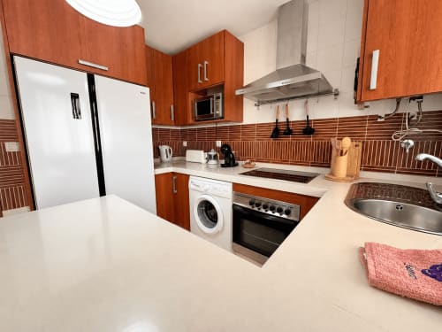 Cocina moderna con muebles de madera, electrodomésticos de acero inoxidable y azulejos rayados en el apartamento Aroma de Poniente de Living
