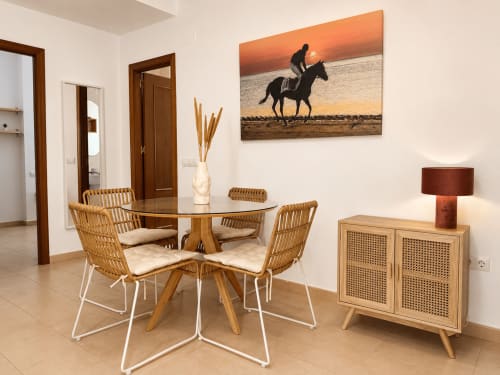Comedor moderno en apartamento Living Sur con mesa redonda, sillas de ratán, mueble de madera y obra ecuestre en Sanlúcar de