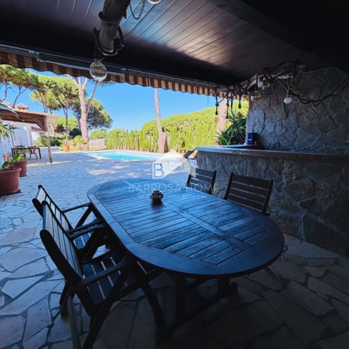 Patio cubierto con mesa de comedor azul y sillas con vistas a piscina privada y jardín exuberante en Villa Irlanda, Chiclana de la