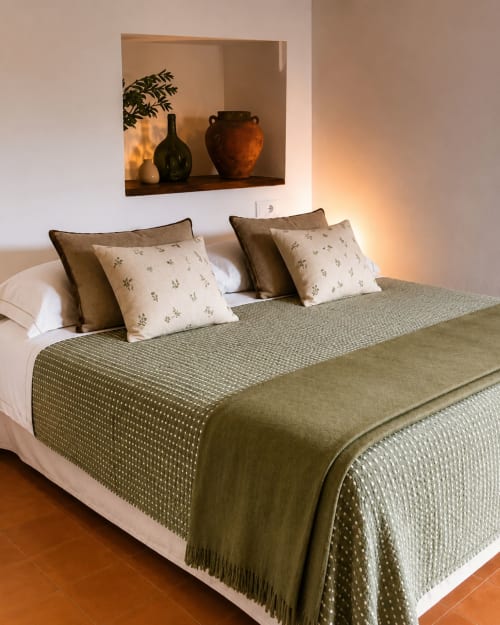 Mas Ribas Hotel bedroom in Palamós with green bedding, decorative pillows, and wall-mounted niche displaying pottery and