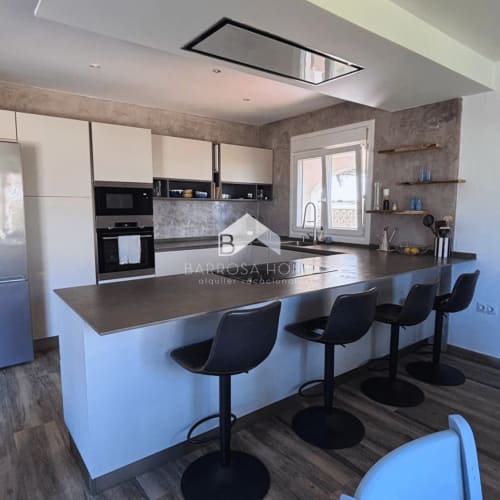 Cocina moderna con isla, taburetes negros y toques de hormigón gris en Villa Irlanda, Chiclana de la Frontera
