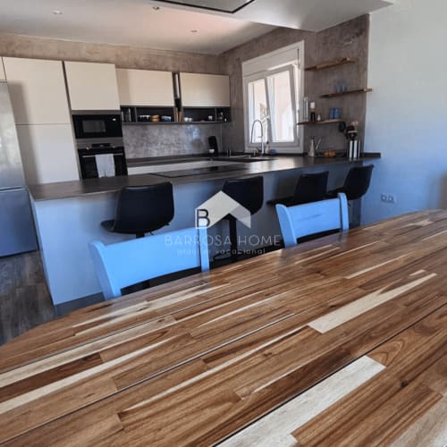 Moderna cocina y comedor en Villa Irlanda de Barrosa Home, Chiclana de la Frontera, con barra negra y detalles de madera