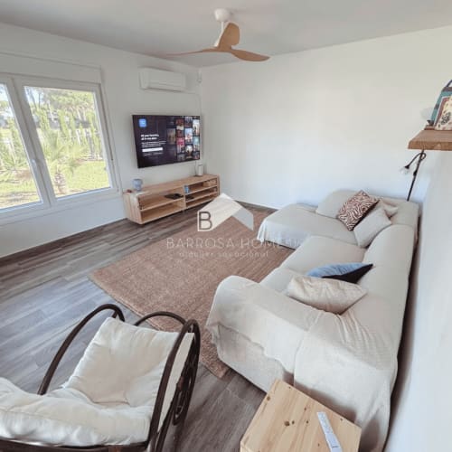 Sala de estar moderna de la villa Barrosa Home con sofá crema, televisor, muebles de madera y vistas al jardín en Chiclana