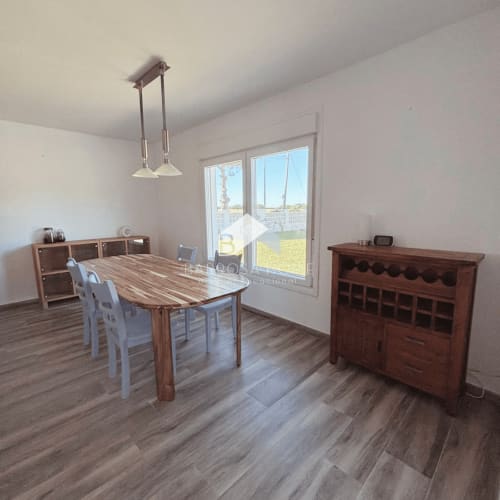 Comedor moderno en Villa Irlanda, Chiclana de la Frontera, con mesa de madera, sillas blancas y vista al jardín a través de cristaleras