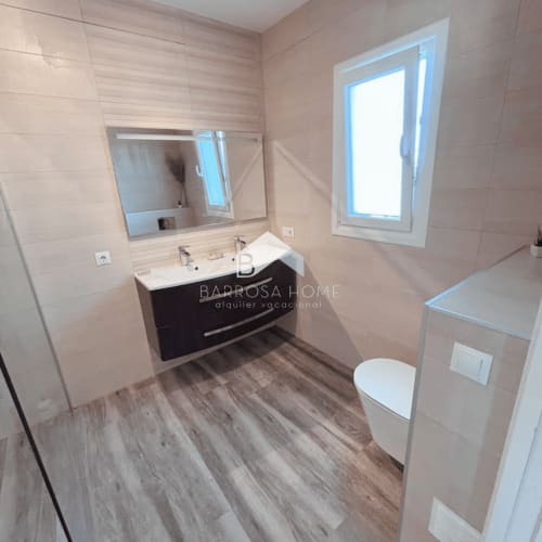 Baño moderno en Villa Irlanda, Barrosa Home, Chiclana de la Frontera con vanidorio negro, espejo, inodoro y acabados tipo madera