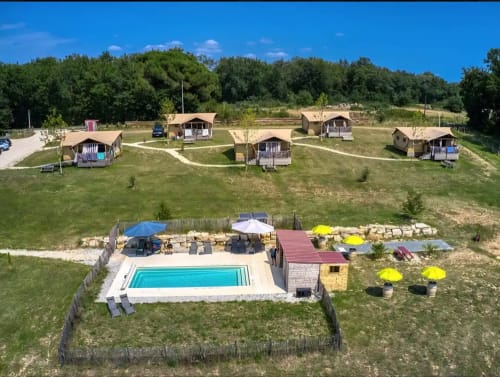 Site de glamping avec piscine, parasols jaunes et cabines rustiques dans les champs verts de l'Aquitaine