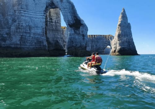 Jet ski riders explore turquoise waters near dramatic white cliffs at Étretat, near Clos Céleste in Normandy
