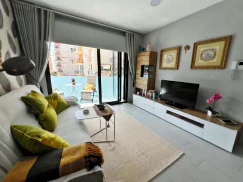 Elegante apartamento de lujo en Fuengirola con balcón, sofá con cojines verdes, televisor y muebles contemporáneos.